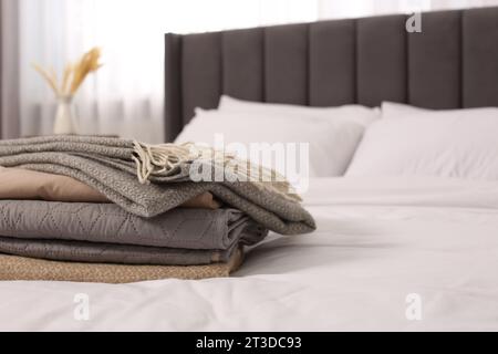 Stack of different folded blankets on bed in room, space for text. Home textile Stock Photo