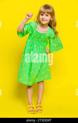 Knock-knock who is there. Confused young blonde child girl kid knocking door gesture asking who is at home, feeling embarrassed, no idea, being clueless uncertain. Little preteen children. Vertical Stock Photo