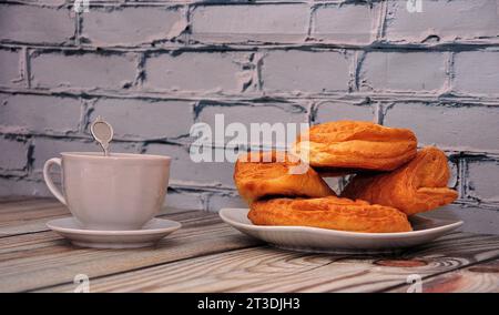 A plate with several fresh puff pastries and a cup of hot drink on a wooden table. Close-up. Stock Photo