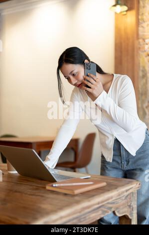 A professional and focused millennial Asian businesswoman is having a business conversation over the phone, talking with someone on her phone while le Stock Photo