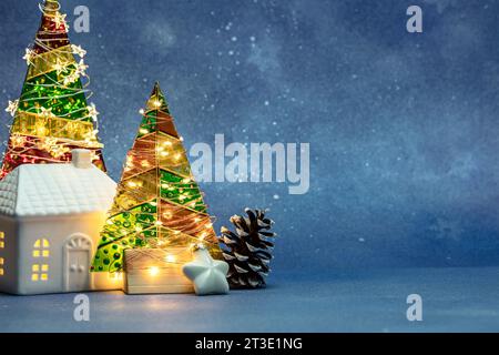 christmas background with illuminated fir trees, toy house and pine cone. blue blurred background with copy space. Stock Photo