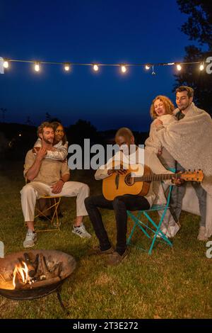 Young hipster people having fun to music dining and drinking together in campsite - Travel vacation lifestyle and youth culture concept, Happy friends group toasting beers at barbecue camping party. High quality photo Stock Photo