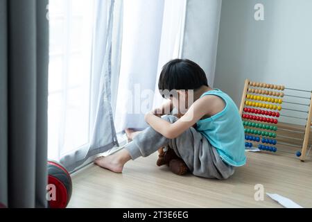 Sad Asian boy sits with his head down and looks out the door at his favorite doll. Stock Photo