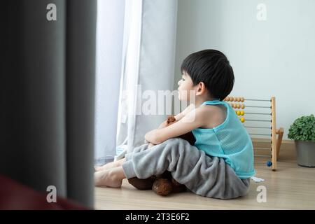 Sad Asian boy sits with his head down and looks out the door at his favorite doll. Stock Photo