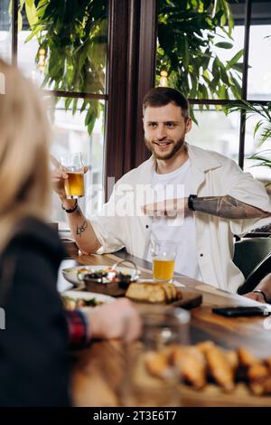 Happy young man drinking draft beer while having fun in pub or bar with friends and laughing Stock Photo