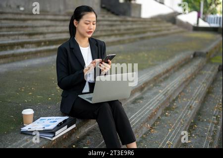 A professional and concentrated millennial Asian businesswoman is texting someone, checking emails, or responding to an urgent message while sitting o Stock Photo