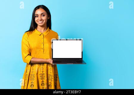 Indian woman showing laptop posing in traditional yellow dress, studio Stock Photo