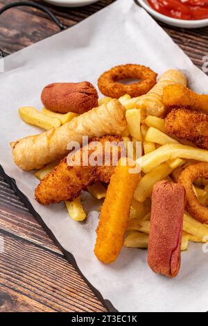 Snack plate with french fries, crispy chicken, cheese sticks, sausage and spring rolls on wooden table Stock Photo