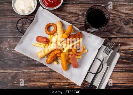 Snack plate with french fries, crispy chicken, cheese sticks, sausage and spring rolls on wooden table Stock Photo