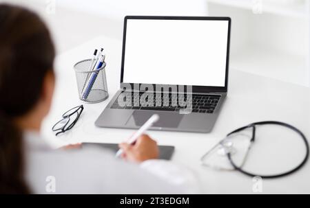 Over shoulder view of woman doctor using laptop, tablet Stock Photo