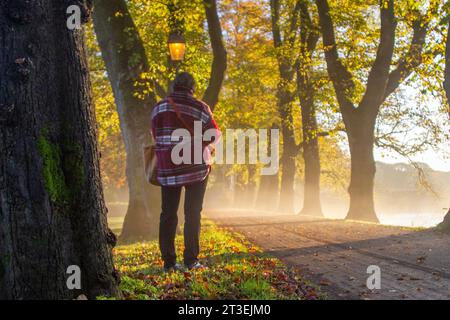 Preston, Lancashire.  UK Weather. 25 Oct 2023.  Fine bright but misty start to the day as the autumn sun rises over the River Ribble. Local residents take light exercise along the tree-lined riverside walk in Avenham Park.   Credit MediaWorlImages/AlamyLiveNews Stock Photo