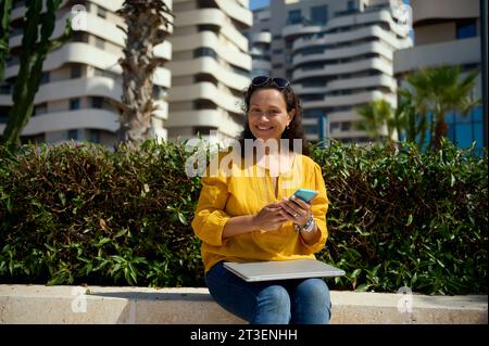 Authentic portrait of beautiful African American young adult woman in casual clothes, a student or entrepreneur using smart phone, checking new mobile Stock Photo