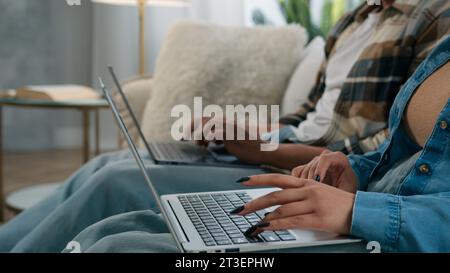 Unrecognizable couple man African woman boyfriend girlfriend guy girl users hackers gamers using two computers working online with laptops at couch Stock Photo