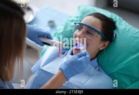 Young woman dentist in protective gloves checking dental seal, fixing photopolymer lamp during stomatology procedure Stock Photo