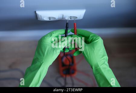 Craftsman in rubber gloves holding tester near electrical outlet at home closeup Stock Photo