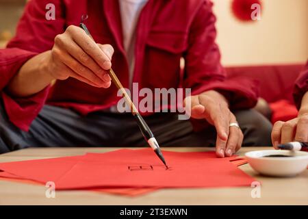 Close up of unrecognizable Asian man writing with ink and brush doing traditional Chinese calligraphy for New Years day, copy space Stock Photo