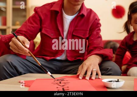 Close up Asian man doing traditional Chinese calligraphy for New Years day with family, copy space Peace and safety wherever you go Stock Photo