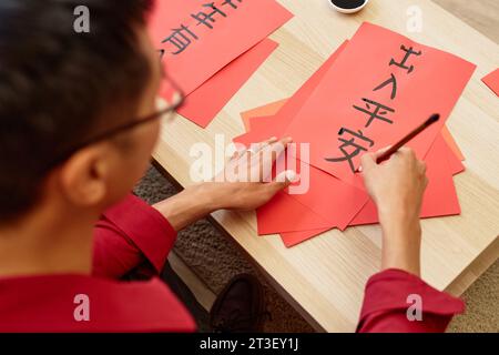 High angle closeup of Asian man writing hieroglyphs with ink and brush doing traditional Chinese calligraphy for New Years day, copy space Peace and safety wherever you go Stock Photo