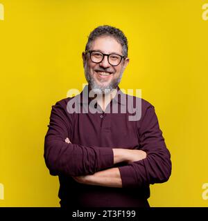 Portrait of a cheerful mature man with glasses and beard, confidently posing against a vibrant yellow background. Stock Photo