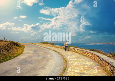 A man walks along the promenade Lighthouse road (Estrada do faro) along the sea on a sunny day Stock Photo