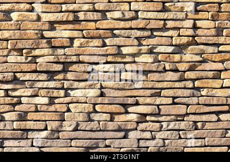 Texture of a wall made of flat old sandstone cobblestones with rounded edges in the sun's rays. Stock Photo