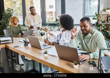 cheerful young friends working actively on their project on laptops and discussing it, business Stock Photo
