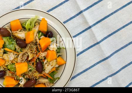 Fresh chicken salad with kalamata olives, cantaloupe melon and sesame seeds. Top view on white kitchen towel with blue stripes. Stock Photo