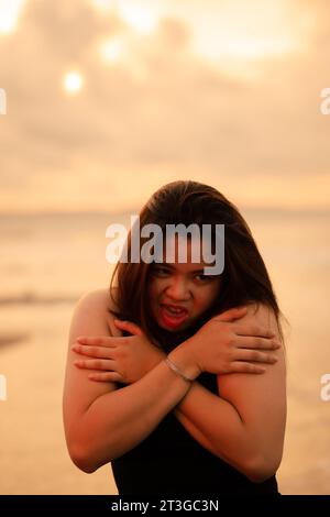 an Asian teenager relaxing on the beach wearing black clothes and posing beautifully in the afternoon Stock Photo