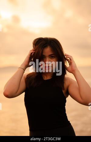 an Asian teenager relaxing on the beach wearing black clothes and posing beautifully in the afternoon Stock Photo