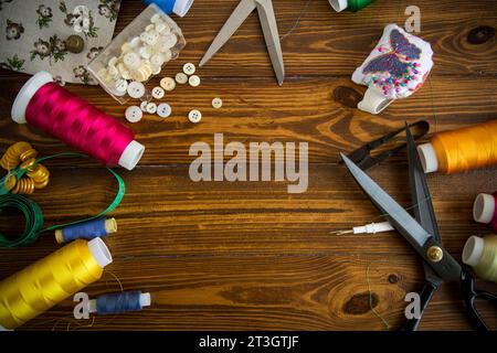 Sewing accessories and fabric on a wooden background. Sewing threads, needles, pins, fabric, buttons and sewing centimeter. Top view, flat lay. High q Stock Photo