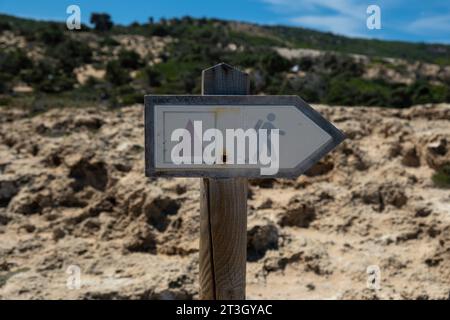 Metal old rusty sign with hiking symbol on wooden pole at Gavdos island, Crete Greece. Direction warning and inform label on blur background. Stock Photo