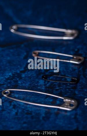 Close-up view of some safety pins, one of which is black in focus and the other three are blurry, on a dark blue background Stock Photo