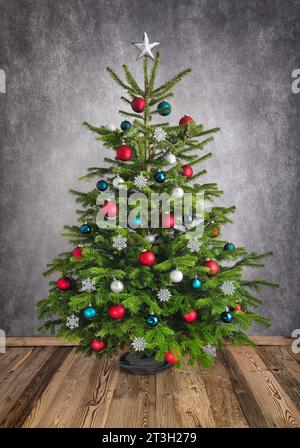 Ornamental Christmas tree on wooden floor with gray textured wall, with red, silver and teal baubles Stock Photo