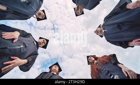 Graduates in black robes stand in a circle. Stock Photo