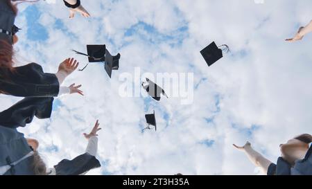 Joyful graduates stand in a circle and toss their caps up. Stock Photo