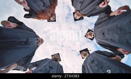 Graduates in black robes stand in a circle. Stock Photo