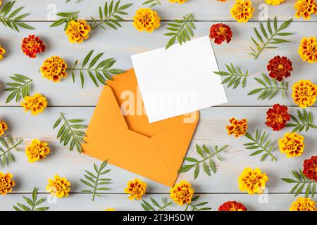 Orange envelope with a white blank sheet of paper for text and orange marigold flowers on a blue wooden table. Festive office desktop concept. Stock Photo