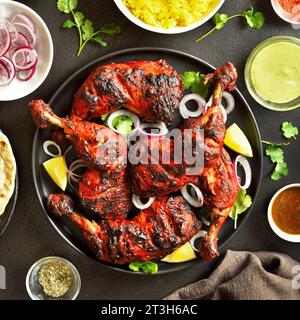 Indian style tandoori chicken on plate over dark stone background. Chicken legs marinated in yogurt and spices. Top view, flat lay Stock Photo