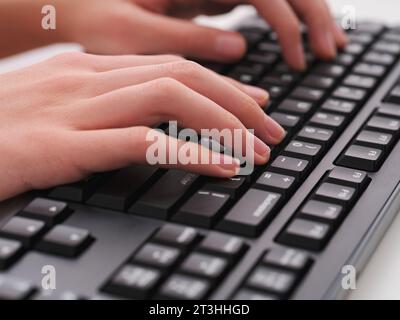 A young man typing on a black computer keyboard. Close up. Stock Photo