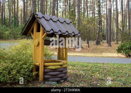 A small log wooden house used as a feeder for small animals. The house stands in a park next to a path. Autumn landscape, yellow fallen leaves. Stock Photo