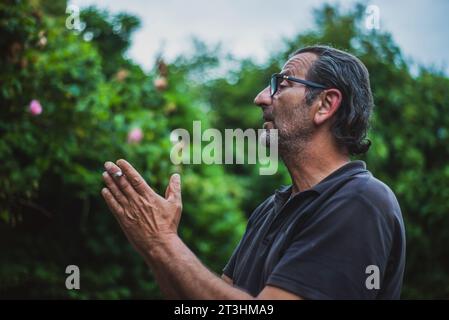 Amidst nature's embrace, a lively 60-year-old Serbian gentleman, wearing glasses and sporting long hair, engages in animated conversations outdoors, h Stock Photo