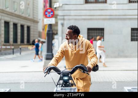 Handsome young African American man in casual wear is looking away while leaning on a bicycle on the street Stock Photo