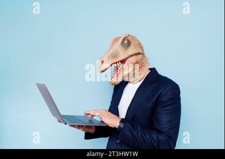 man in dinosaur mask using laptop.Blue background Stock Photo
