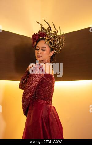 Asian woman in red dress posing with a gold crown on her head inside the studio Stock Photo
