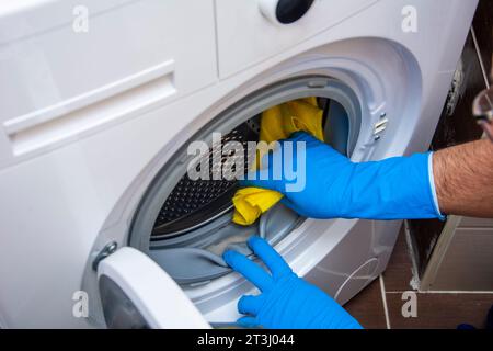 An unrecognizable hand cleans accumulated dirt in the washing machine with a yellow cloth Stock Photo