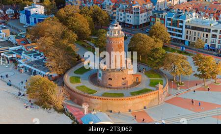 Drone photo captures Kołobrzeg's maritime charm, featuring the iconic lighthouse, cerulean sea, turbulent waves, a distant pier. Stock Photo