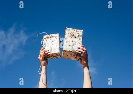 eco-friendly gift boxes with reusable paper wrappings and string ribbon, attached to hands over blue sky Stock Photo