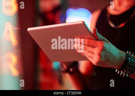 Hands of young stylish man with tablet standing in front of camera in cyberpunk bar or cafe and scrolling through online video games Stock Photo