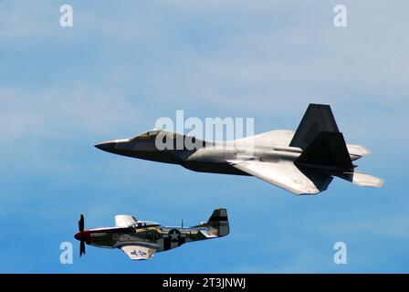 Representing two eras in flight, a World War II P51 Mustang flies side by side with a modern F 22 Raptor military jet plane Stock Photo
