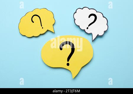 Paper speech bubbles with question marks on light blue background, flat lay Stock Photo